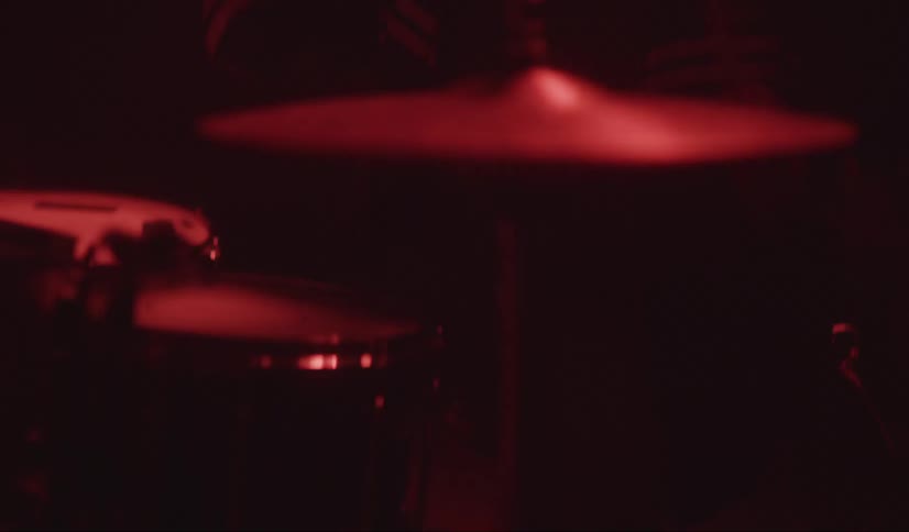 A man bobs his head while playing the drums in a dark room under a red light