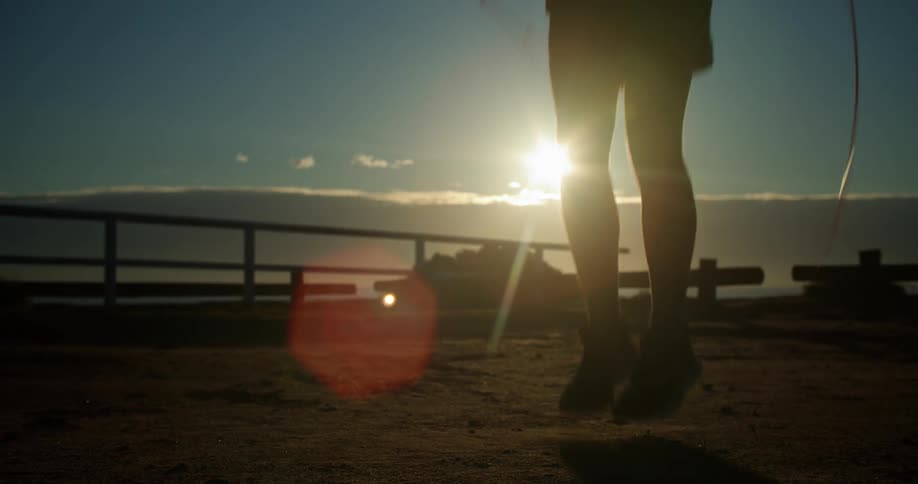 A man jumps rope on the beach at sunset