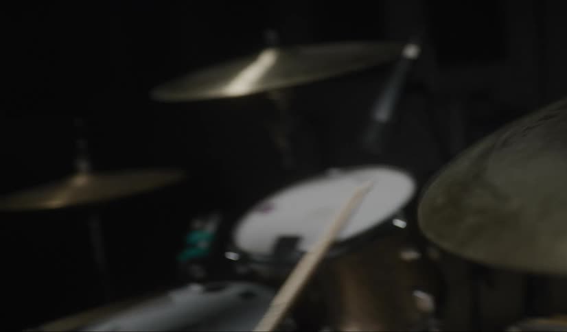 Drummer wearing earphones plays drums in dimly lit room