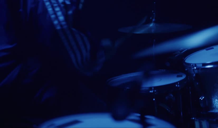 A man is playing the drums on the dark stage