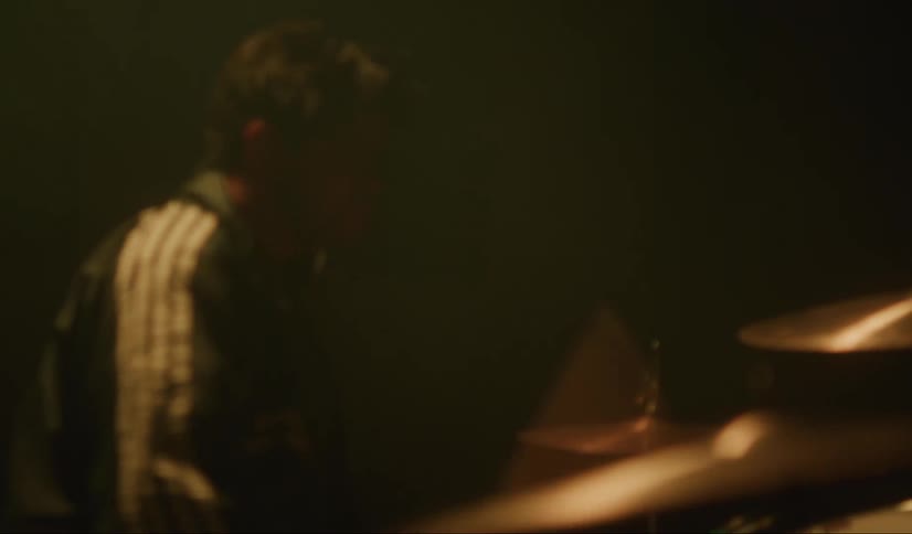 Smiling man plays drums sitting under lights on dark stage