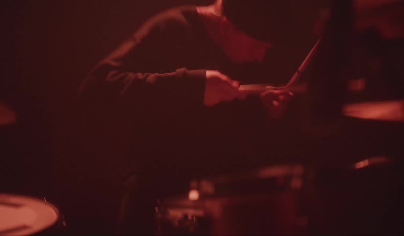 A man bobs his head while playing the drums during an indoor performance