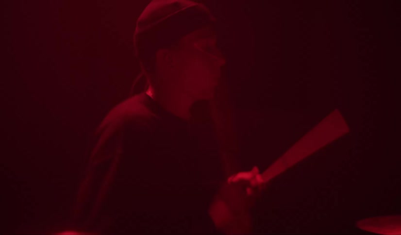 A male drummer rapidly strikes drums and cymbals with his drumsticks