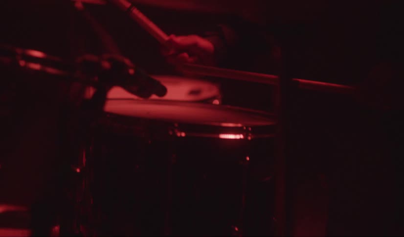 Drummer with beard plays drums under red colored lights