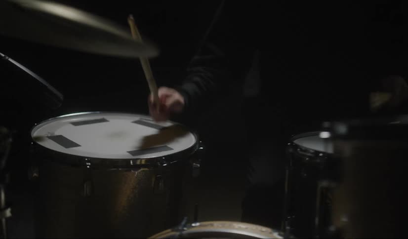 Man energetically plays drums on dark stage under strobing lights