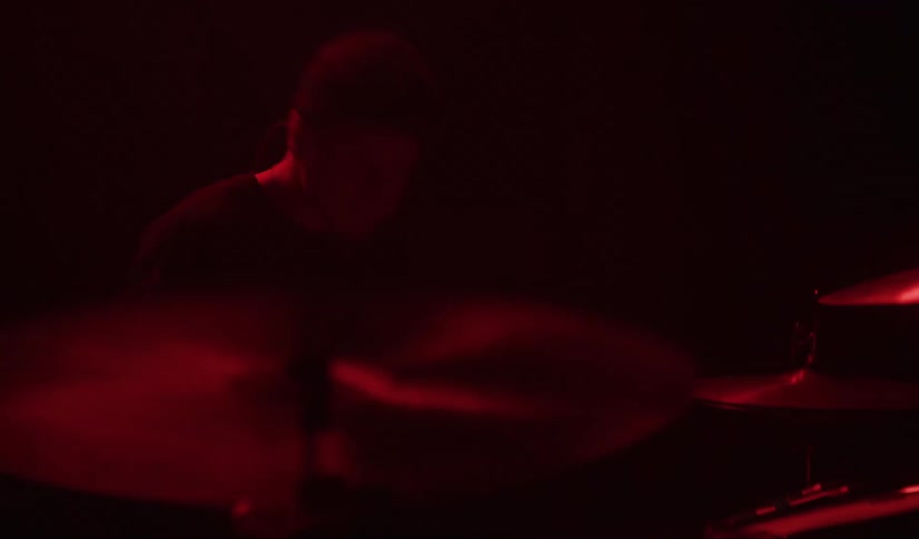 A male drummer quickly strikes his drums and cymbals in a darkened environment