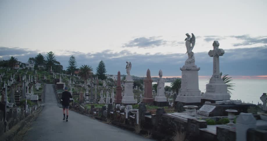 A man jogs on a trail that runs through a cemetery along the ocean