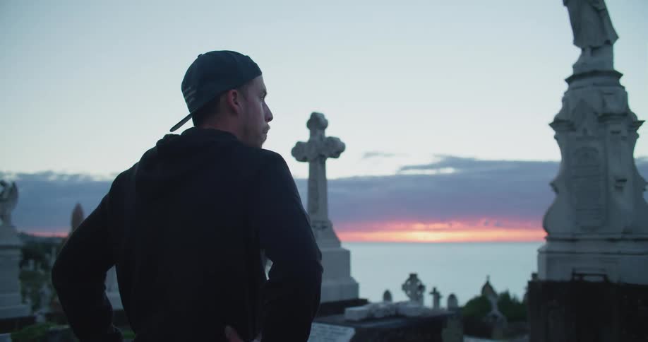 Man wearing his hat backwards stands looking at monuments and the lake at sunset