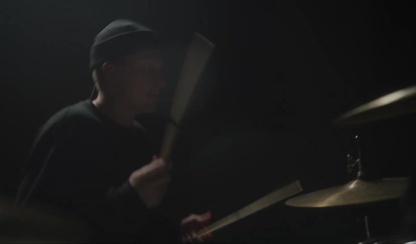 Wires lead across floor to drummer playing drum set on dark stage