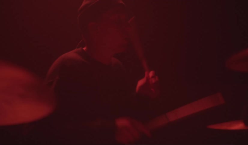 Man wearing a toque plays the drums and cymbals with drumsticks while nodding his head to the beat