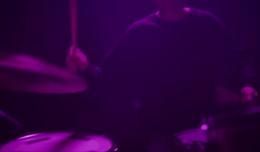 A drummer plays in a dark room under color changing lights