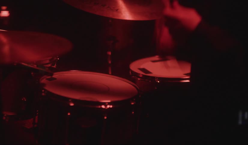 A drummer plays the drums under a flashing red light in a dark room