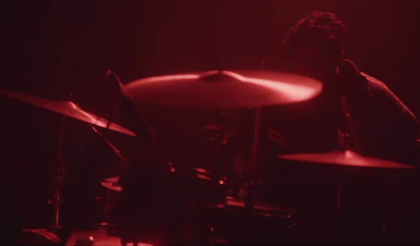 A musician playing drums in a dark room with red lighting