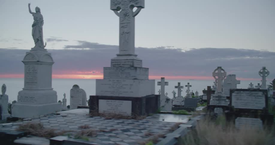 Graveyard monuments contrast against ocean and red tinted horizon