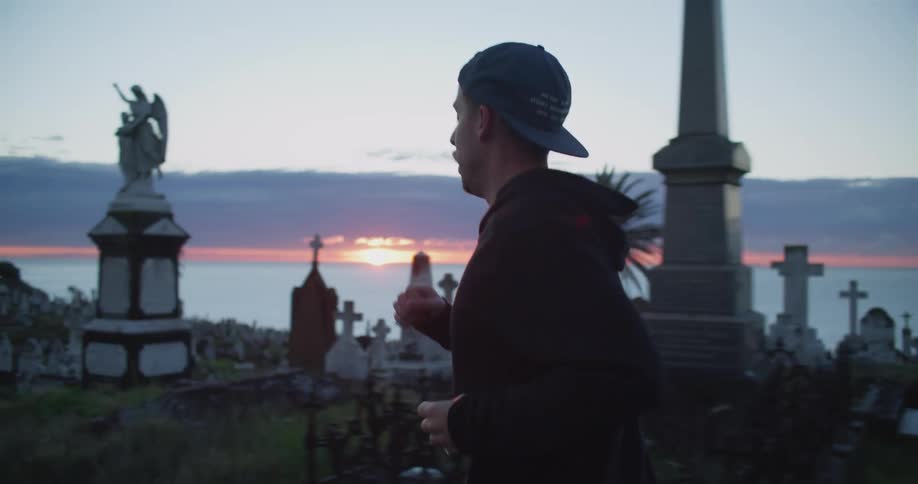 Man jogs along street through graveyard as sun turns horizon over ocean red