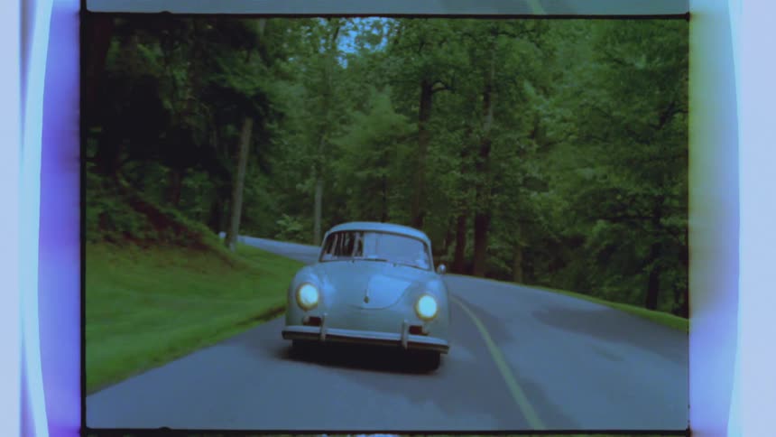 An older blue car travels down a road