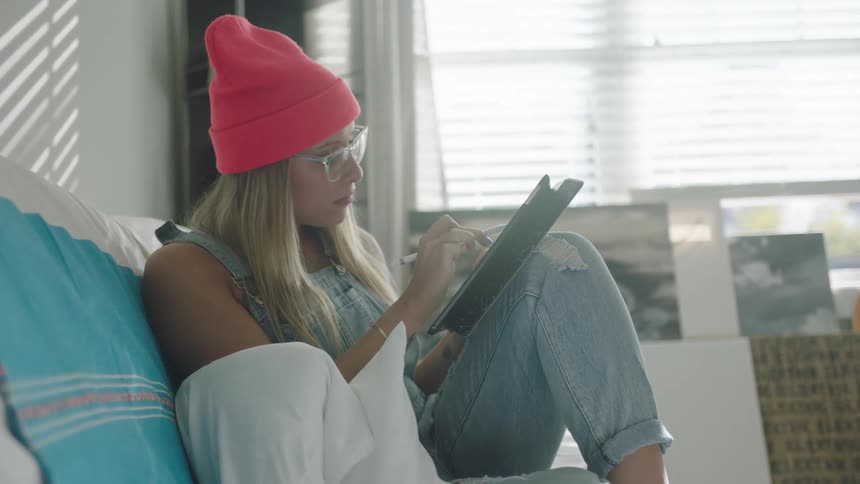 A woman is sitting on the couch and on a tablet