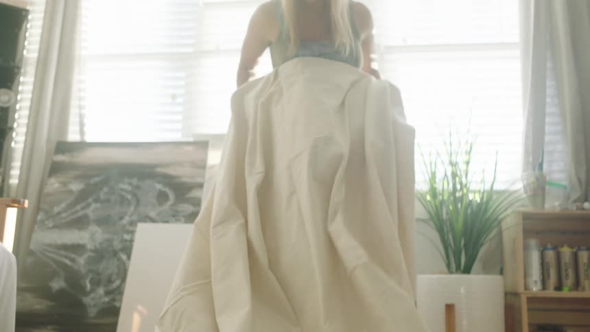 A woman wearing overall unfurls a large drop cloth as she prepares to paint