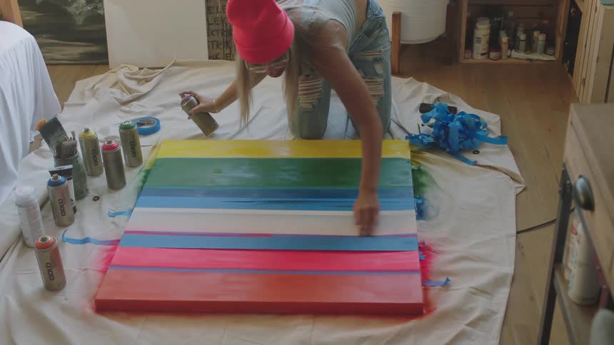 A woman uses painters tape and spray paint to make a striped piece of art