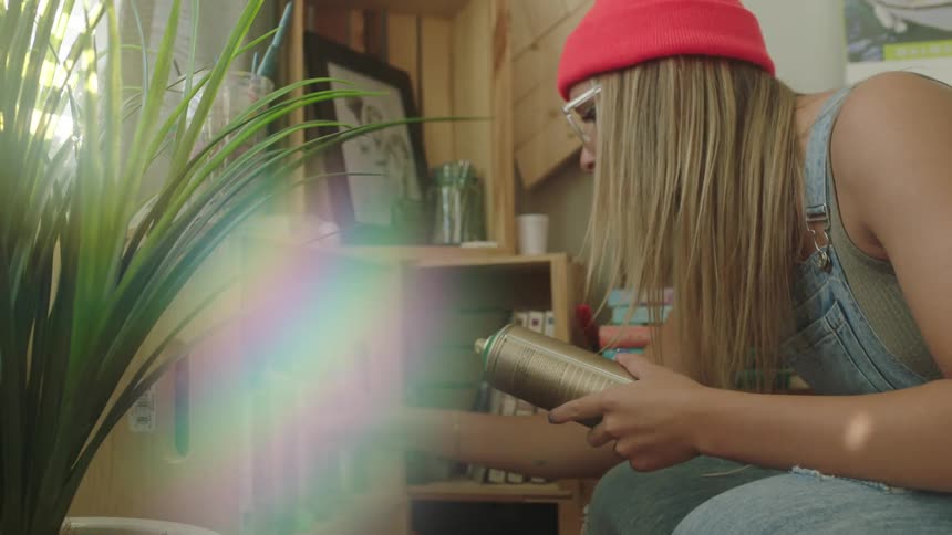 A woman crouching down selecting spray paint cans from a shelf in her home