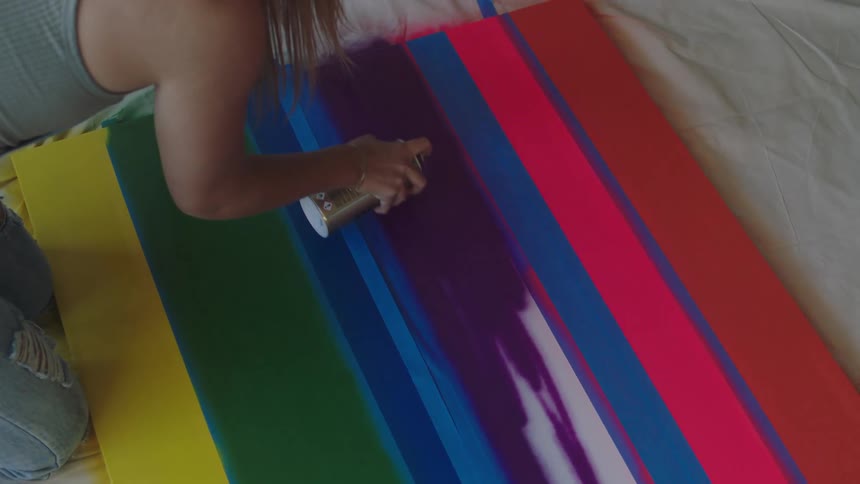 A woman uses painters tape and spray paint to create a large piece of art