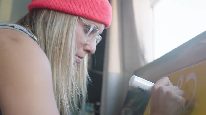 A woman uses a paint marker to write on a poster