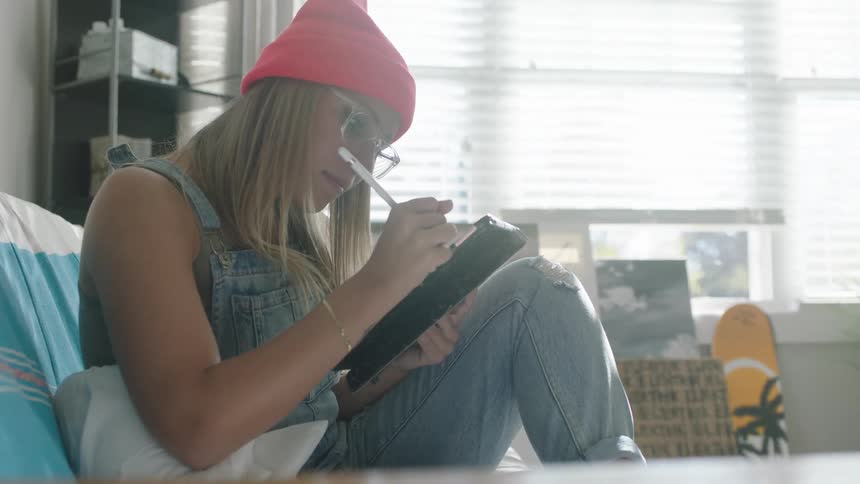 Woman sits on couch drawing with stylus on tablet