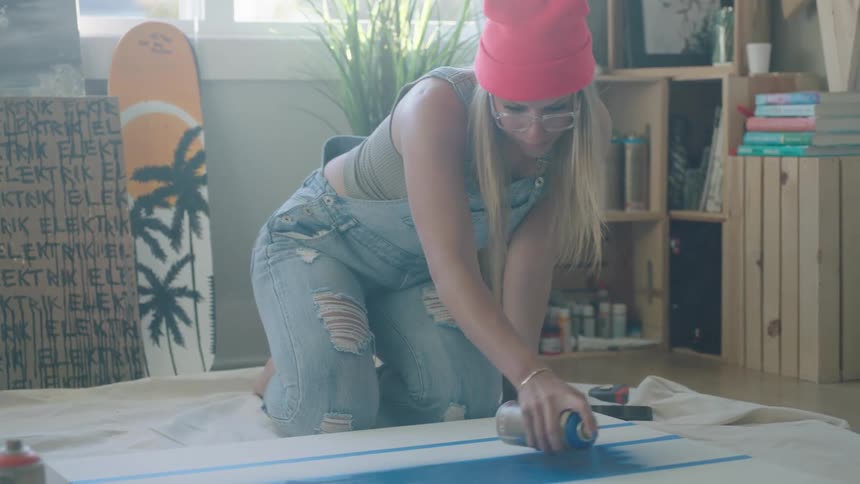 A woman spray paints a large white board in her living room