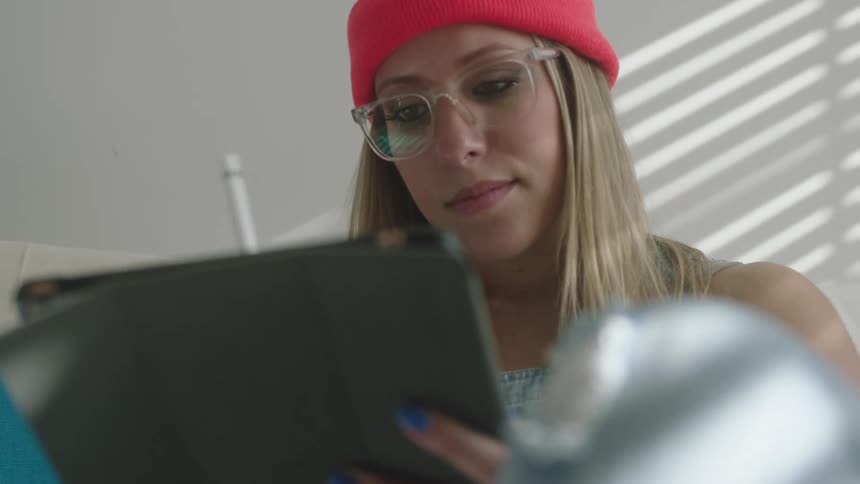 Woman walks across living room to sit on couch drawing on tablet with stylus