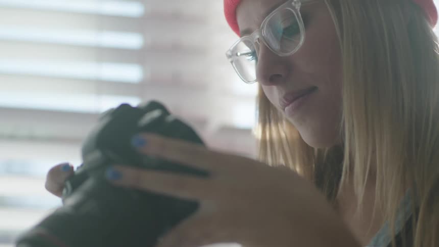 A woman holds a camera with a long lens and she inspects some of the settings