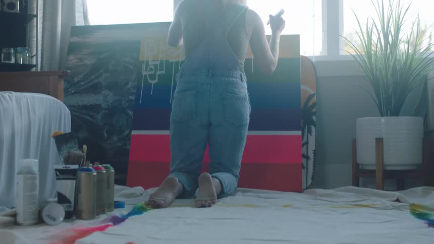 A woman in a room painting on a canvas with a window in the background