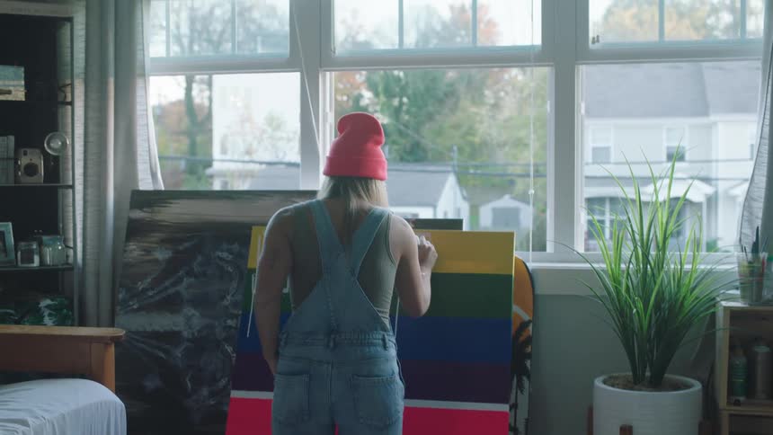 A woman in a room painting on a canvas with a window in the background