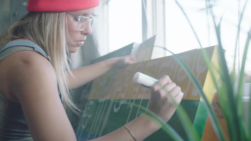 A woman adds white paint shapes onto a color blocked canvas