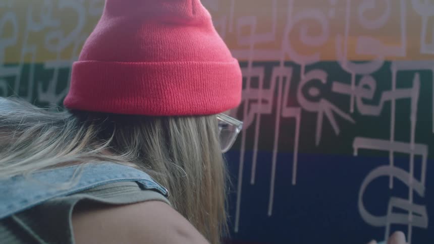 A woman kneels to write on a colorful board beneath a window with a white marker