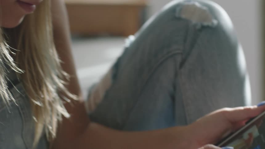 A woman with a hat and glasses sitting on a couch using a tablet with a stylus