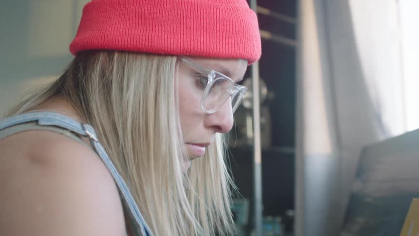 Blonde female artist marks painted canvas with sponge tipped paint bottle pressing to let paint drip