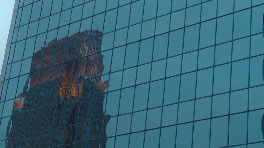 A reflection of buildings off a skyscraper with the sky and clouds in the background