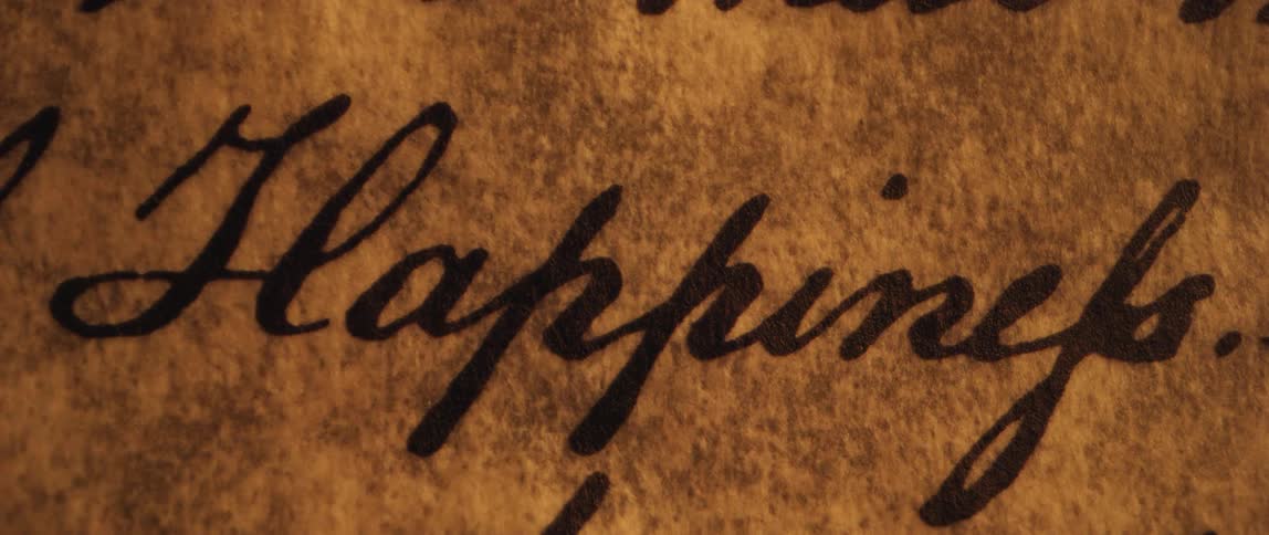 Candle light flickers on parchment with a word written in cursive with ink