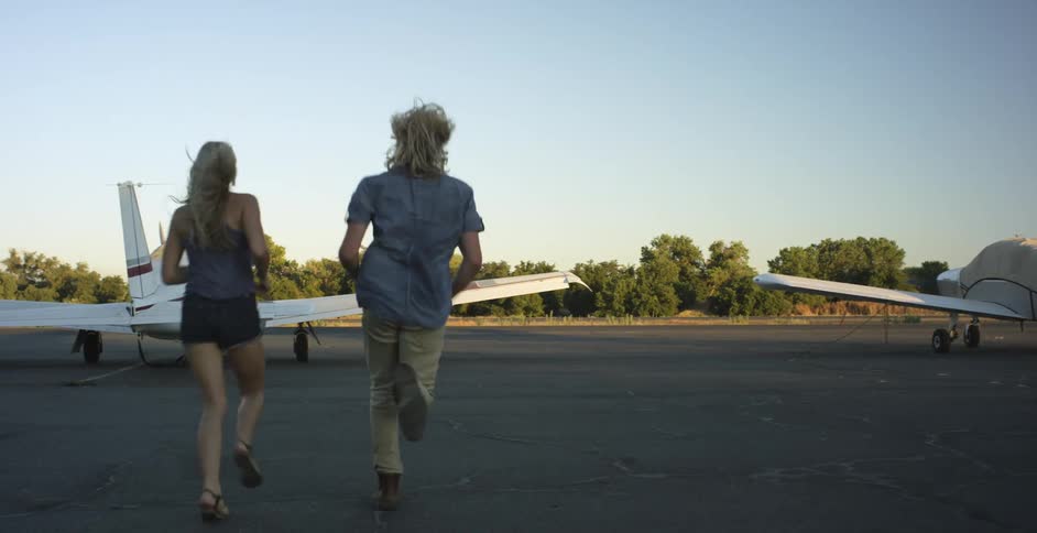 A man and woman are running toward a plane on a sunny day