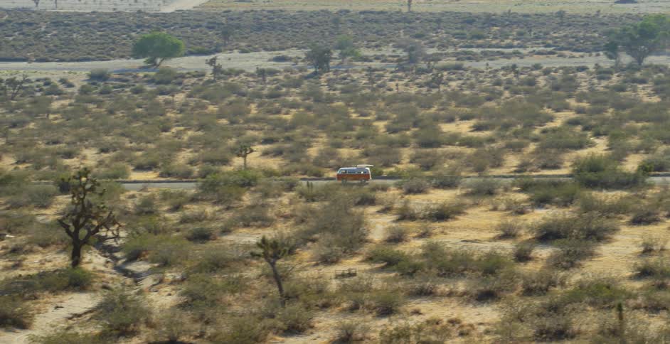 A v.w. is being driven through the desert on a sunny day