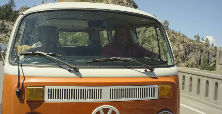 Orange and white van travels down the highway near the mountains