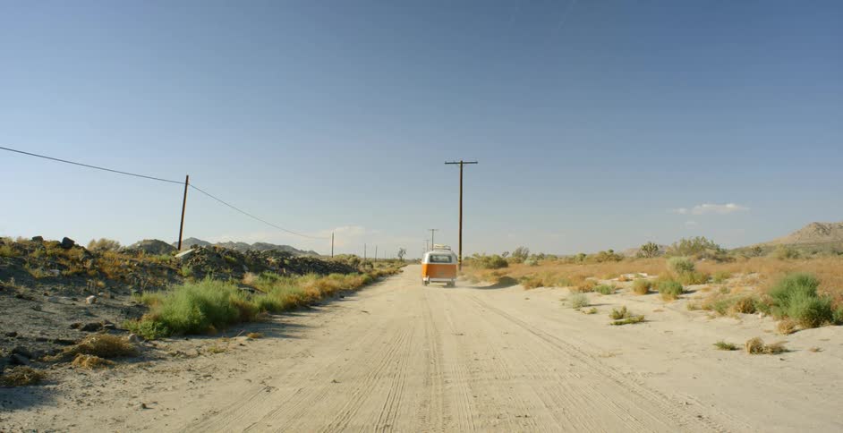 Orange and white van travels down a dirt road