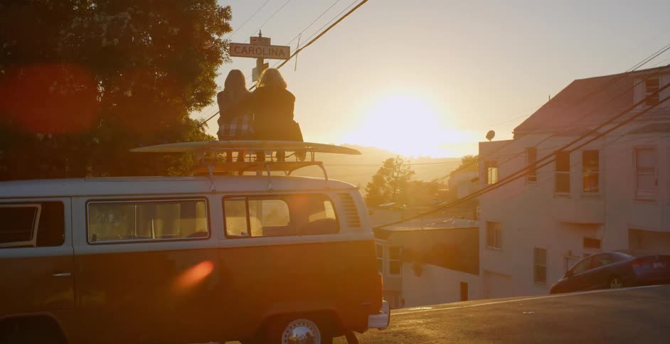 A couple of people are sitting on top of a van looking at the sunset