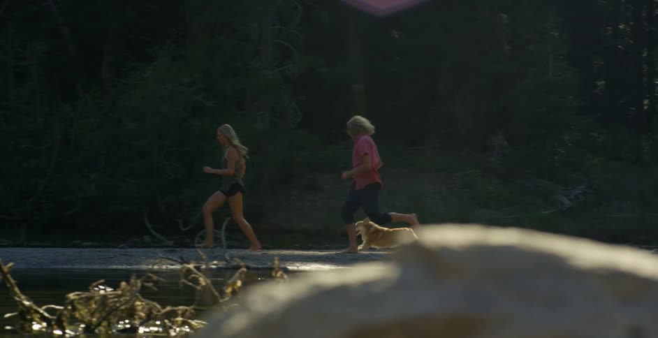 Corgi runs with a man and woman on a lakeshore