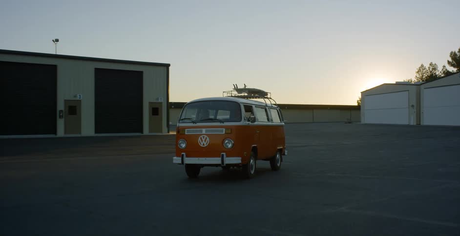 A van with surfboards on the roof rack travels through a rural airport