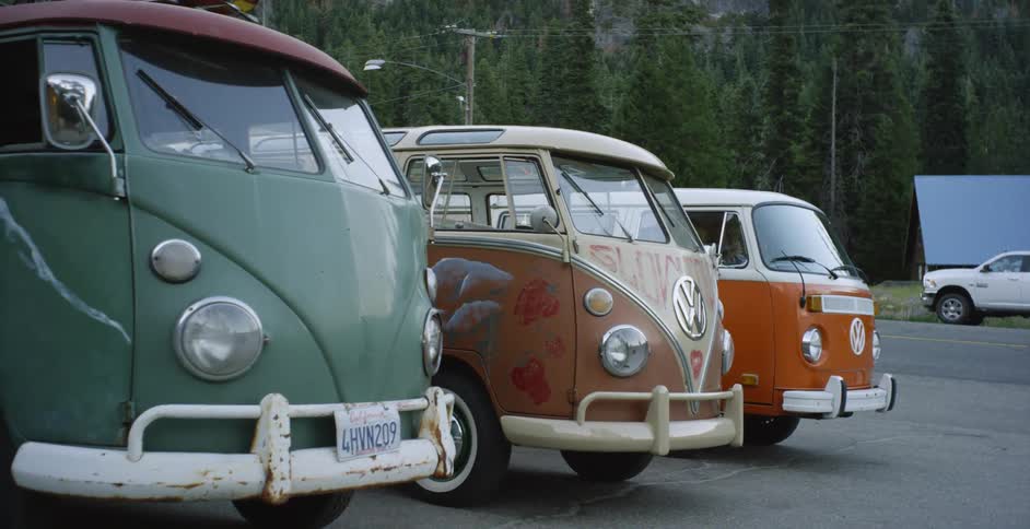 Three Volkswagen vans are parked in a parking lot near a forest area
