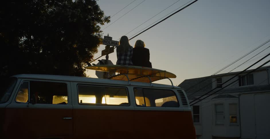 A man and woman are sitting on top of their vehicle watching the sun set