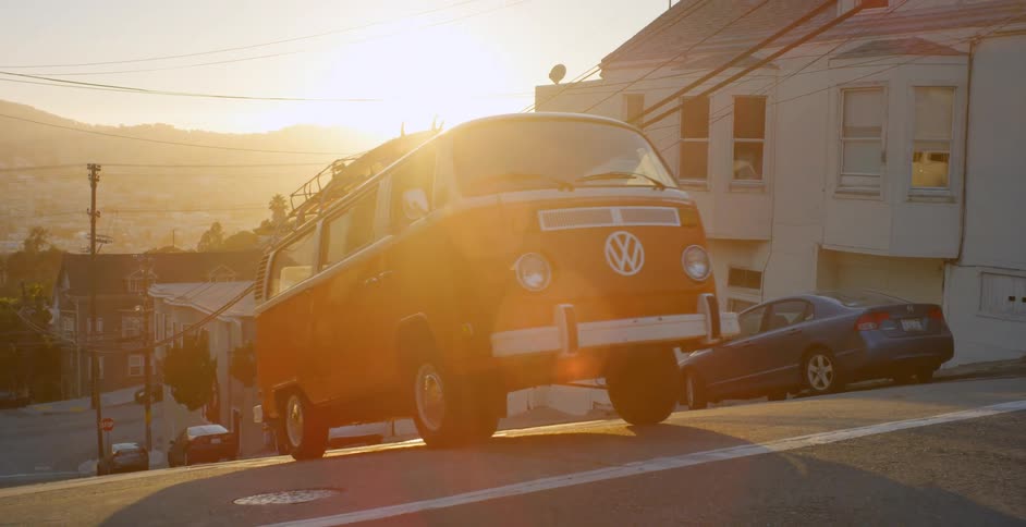 A v.w. bus is driving up a hill in a city in daylight