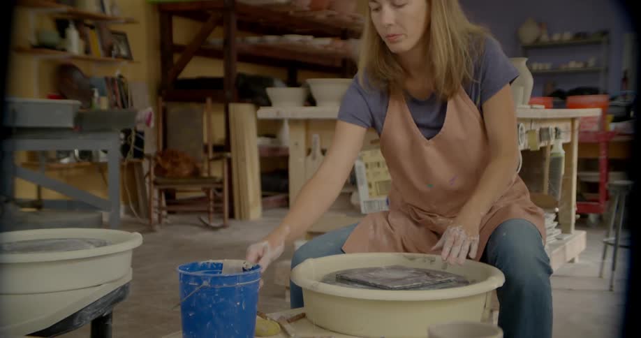 A woman is sitting down near a clay wheel