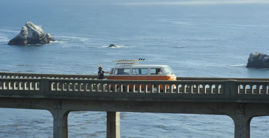 An orange van travels on a bridge over a river